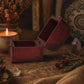 Petit coffre à bijoux bordeaux ouvert, intérieur laqué et charnières apparentes.
