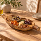 Coupe en teck en forme de feuille garnie de crackers, olives, fromage et fruits secs