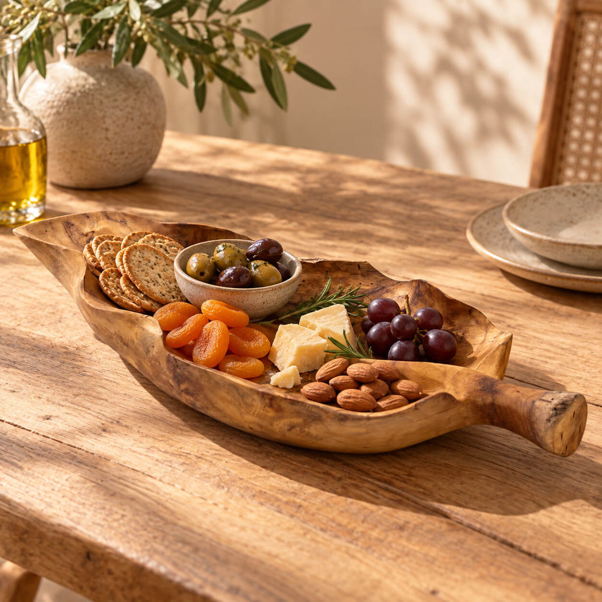 Coupe en teck en forme de feuille garnie de crackers, olives, fromage et fruits secs