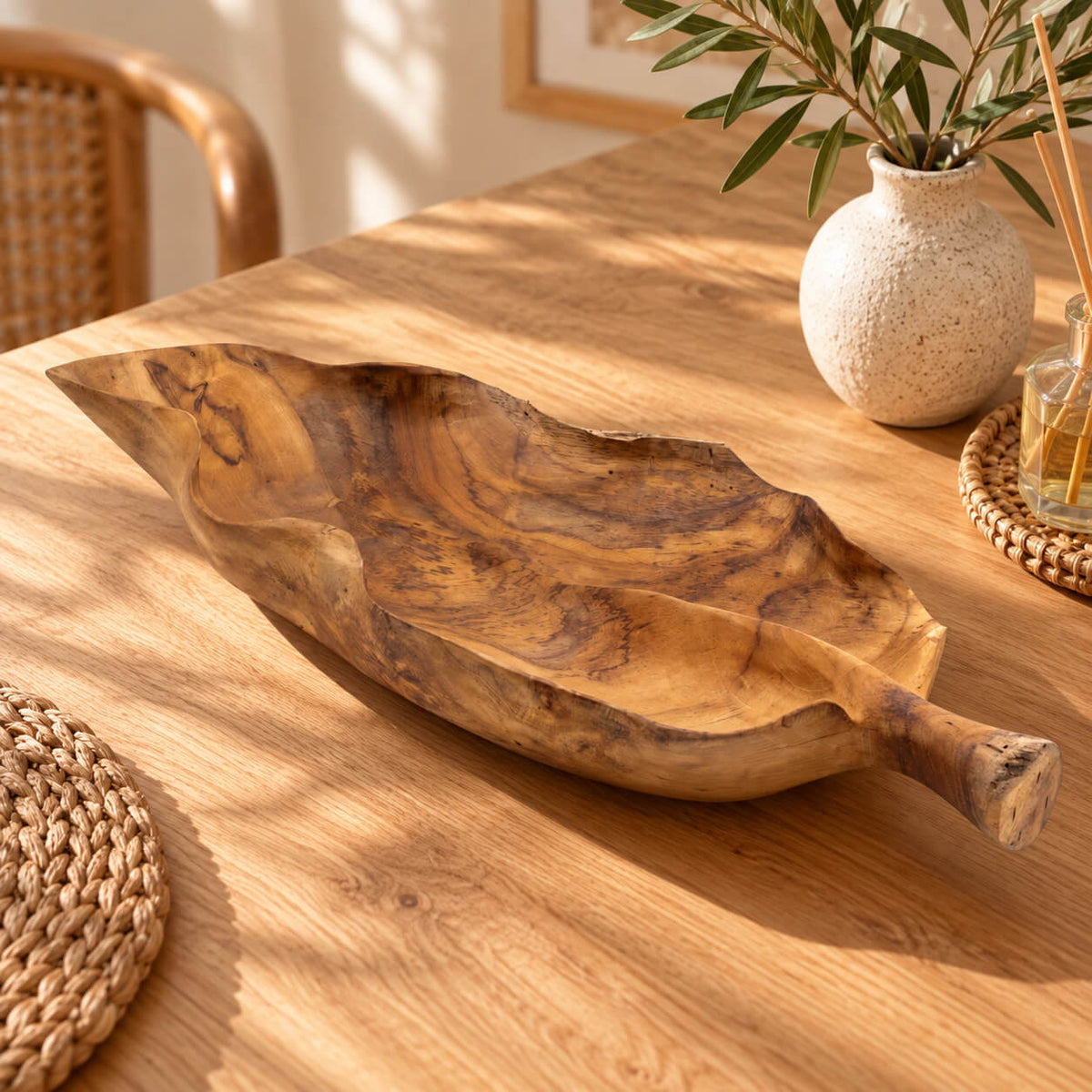 Coupe en teck vide en forme de feuille avec poignée sculptée, posée sur une table en bois