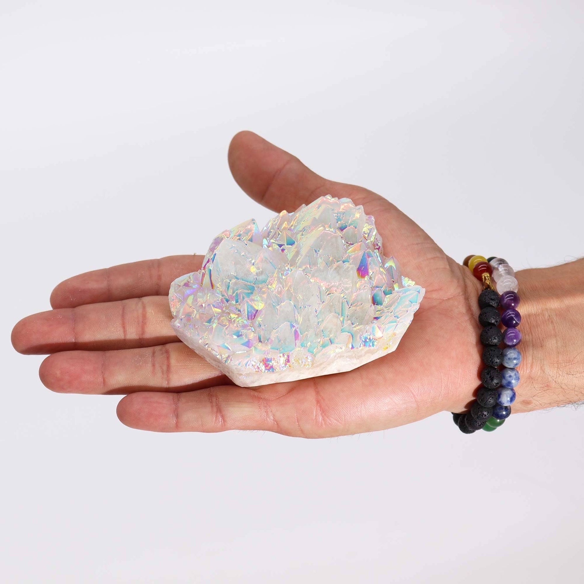 Un Quartz Aura Angélique tenu dans une main de couleur brun profond, offrant une échelle visuelle pour ce cristal de taille moyenne. Le quartz reflète des couleurs iridescentes sous la lumière, mettant en valeur le traitement aura unique et la structure naturelle du cristal.