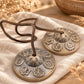 Paire de cymbales tingsha en laiton patiné, dôme en lotus et sept chakras en relief, posées sur du lin avec leur lanière en cuir