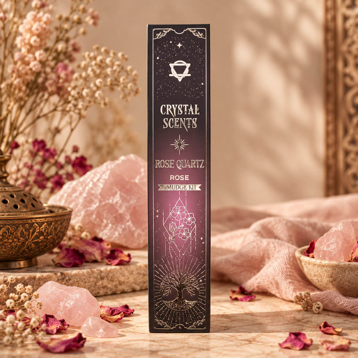 Étui prune et rose d'encens à la rose orné d'un cristal fleuri et d'un arbre de vie dorés, entouré de blocs de quartz rose brut