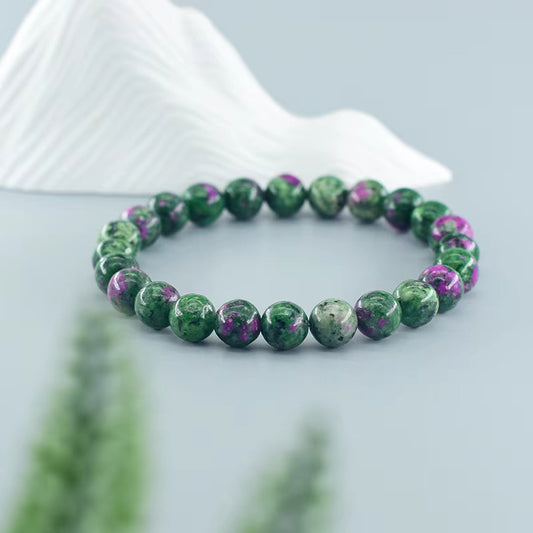 Bracelet en épidote présenté devant un fond stylisé de montagnes, affichant les perles de 8mm aux nuances vert profond avec des inclusions rose-violacées caractéristiques.