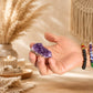 Petite grappe d'améthyste naturelle tenue dans une main avec bracelets en pierres naturelles.