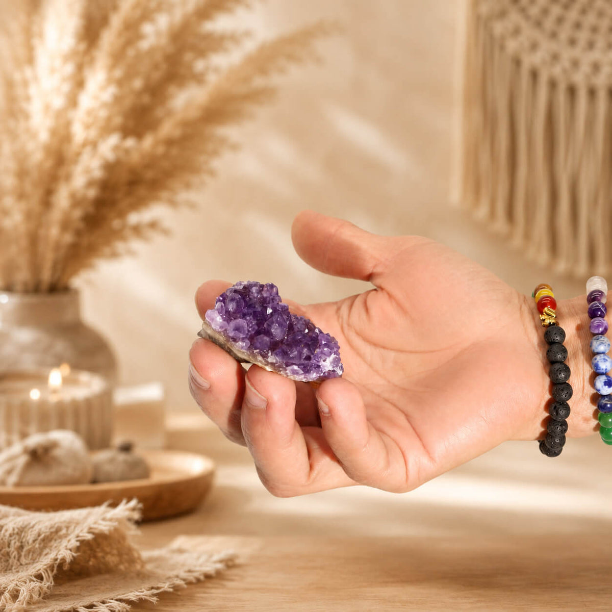 Petite grappe d'améthyste naturelle tenue dans une main avec bracelets en pierres naturelles.