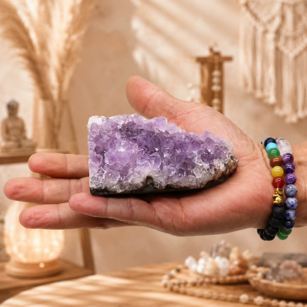 Grappe d'améthyste naturelle moyenne tenue dans une main avec bracelets en pierres naturelles.