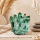 Grappe de quartz fantôme vert aux pointes striées posée sur table claire