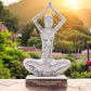 Statue de yoga en bois blanc patiné illustrant une pose d'élévation des bras, sur socle gravé du mantra 'HANDS TO THE HEAVENS EMBRACE PEACE', photographiée au coucher du soleil dans un jardin fleuri