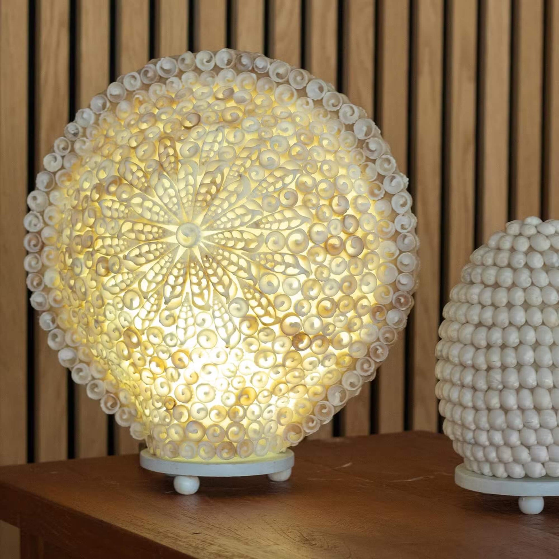 Lampe boho mandala de coquillages marins allumée dans un intérieur scandinave aux lattes de bois.