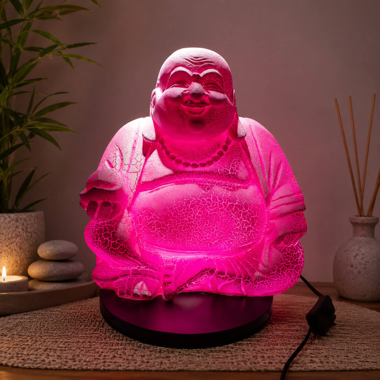 Lampe Bouddha rieur rose vif craquelée allumée diffusant une lumière rose dans un coin détente.
