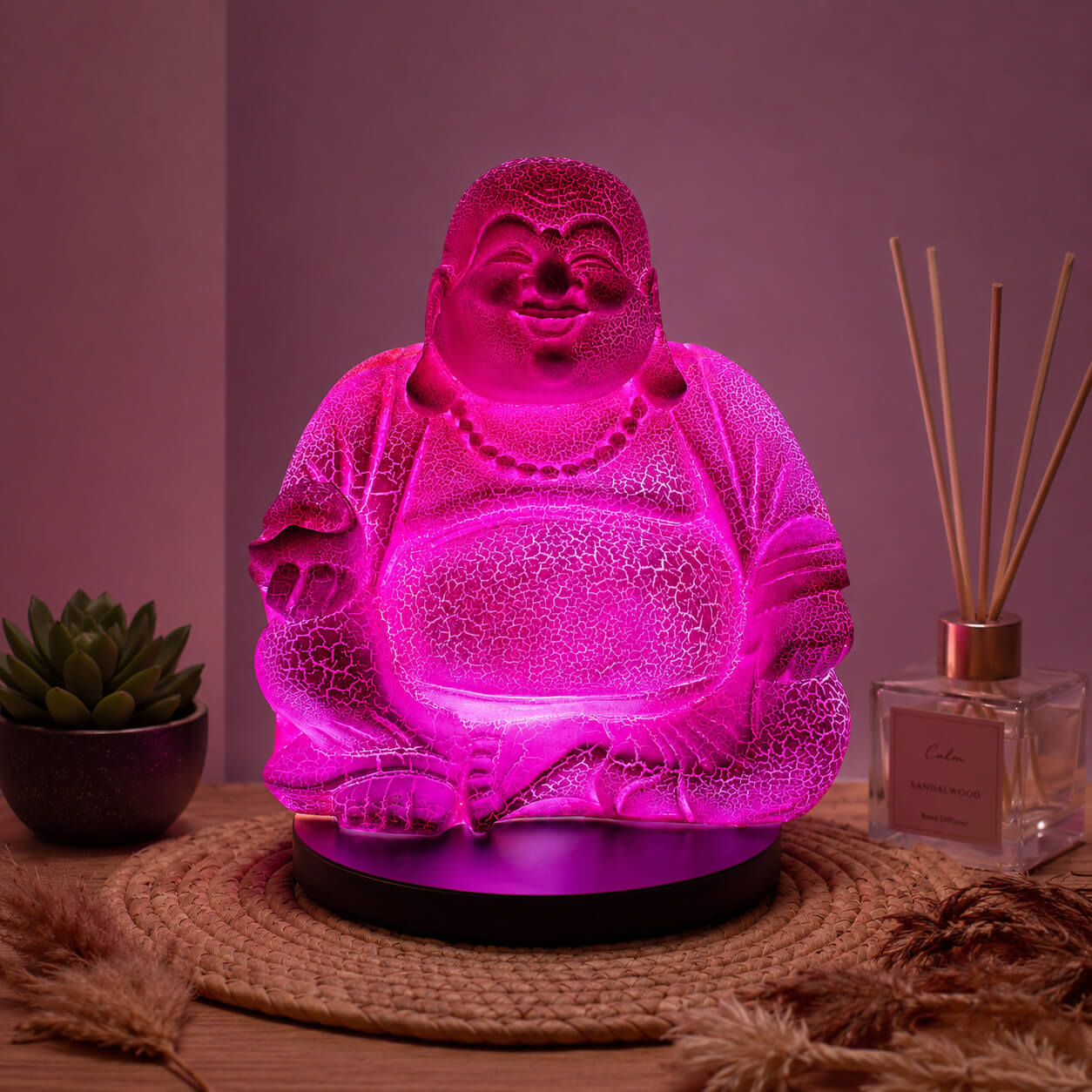 Lampe Bouddha rieur rose vif craquelée allumée dans une ambiance zen.