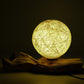 Lampe boule cocon crème allumée diffusant une lumière dorée sur souche bois flotté