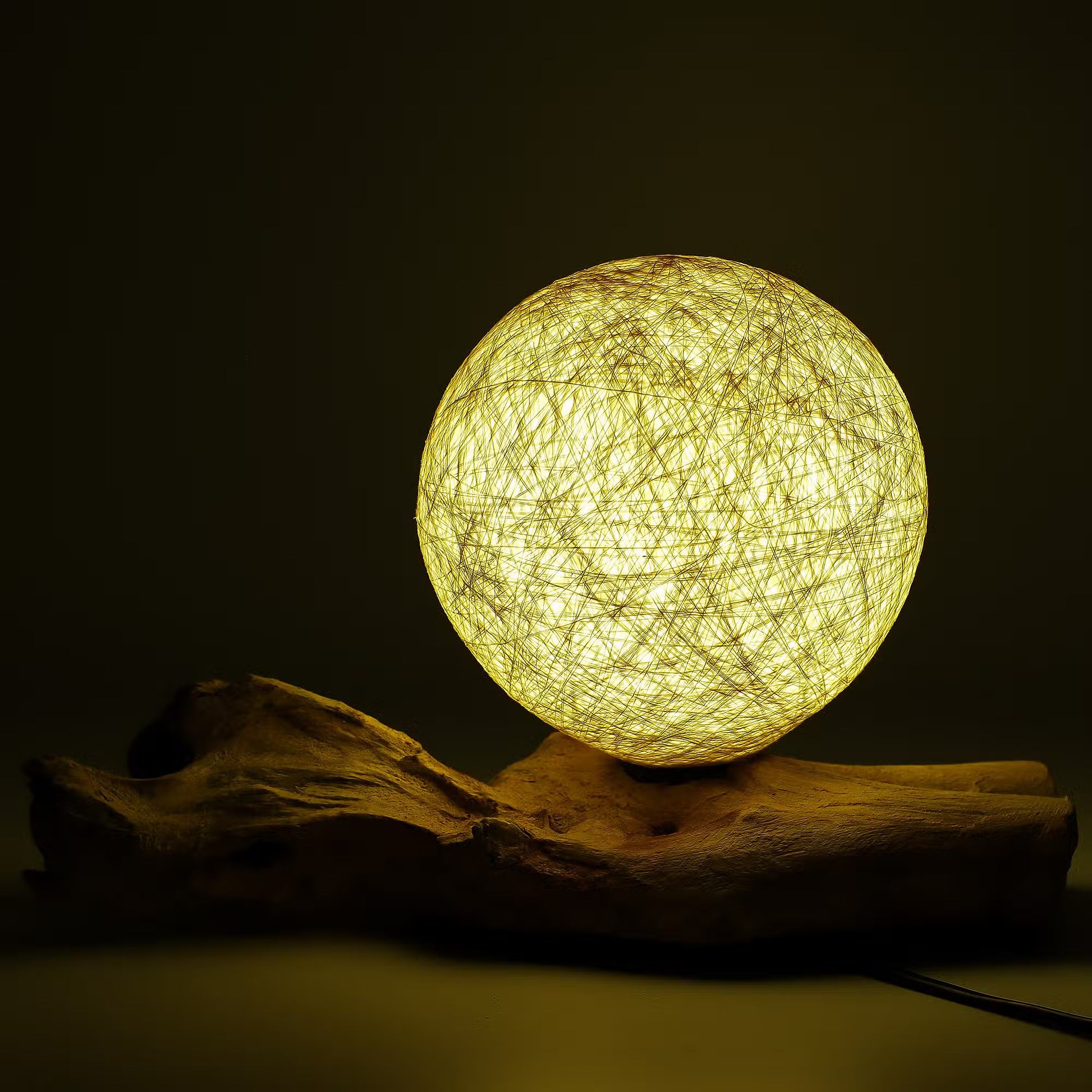 Lampe boule cocon crème allumée diffusant une lumière dorée sur souche bois flotté
