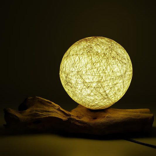 Lampe boule cocon crème allumée diffusant une lumière dorée sur souche bois flotté