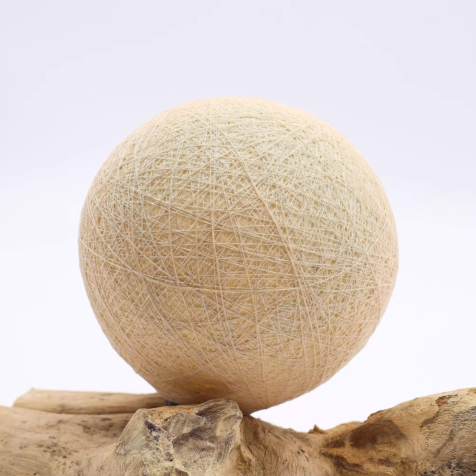 Détail du tissage en fils enroulés crème de la lampe boule sur bois flotté
