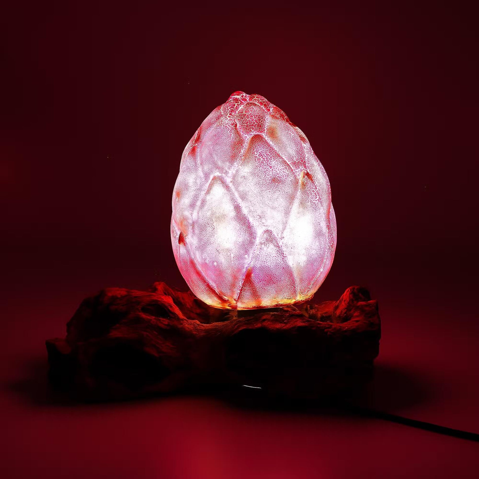 Lampe bouton de lotus rose mauve allumée révélant ses pétales lumineux sur souche bois flotté.