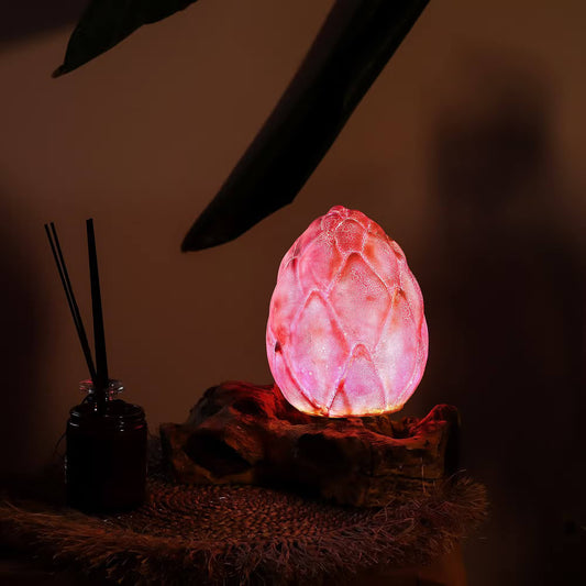 Lampe bouton de lotus rose aux reflets mauves allumée sur table de chevet zen.