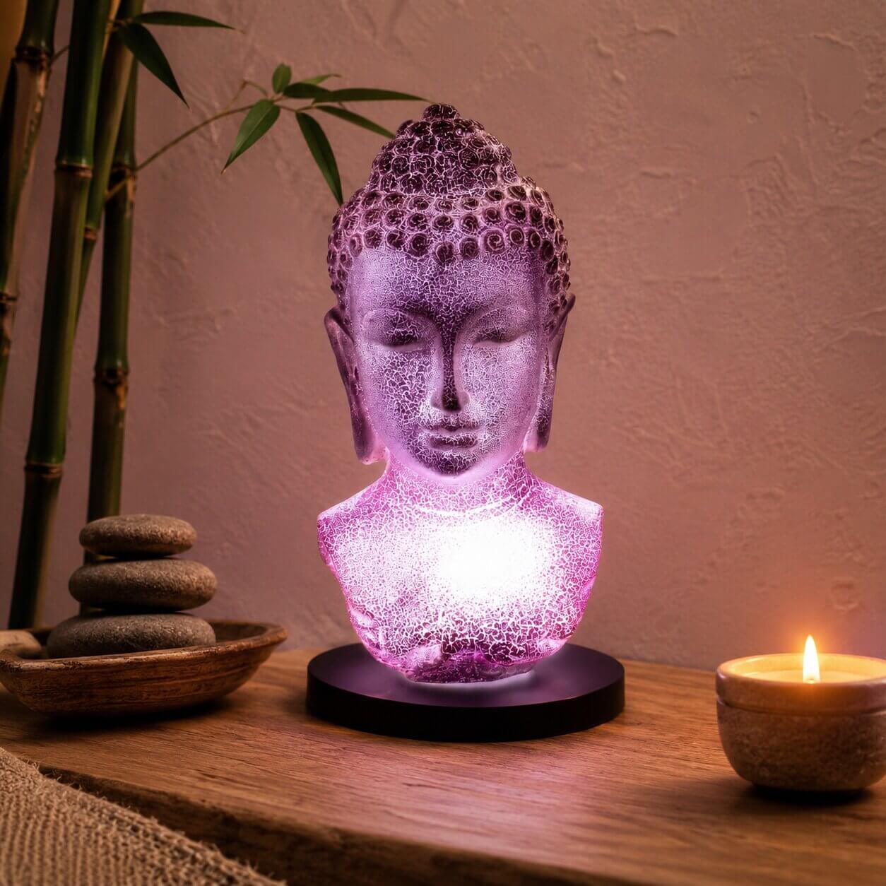 Lampe buste de Bouddha lavande craquelée allumée diffusant une lumière violacée dans un coin méditation.