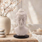 Lampe buste de Bouddha lavande craquelée éteinte sur socle ovale noir en décor naturel.