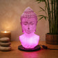 Lampe buste de Bouddha rose craquelée allumée dans une ambiance zen aux bambous.