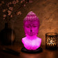 Lampe buste de Bouddha rose craquelée allumée diffusant une lumière rosée dans un coin méditation.