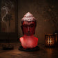 Lampe buste de Bouddha rouge craquelée allumée diffusant une lumière rouge dans un coin méditation.