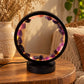 Lampe cercle en améthyste allumée sur une table en bois, reflets violets et dorés