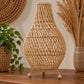 Lampe de table en rotin naturel tressé, forme ventrue sur trois pieds, posée sur un buffet en bois