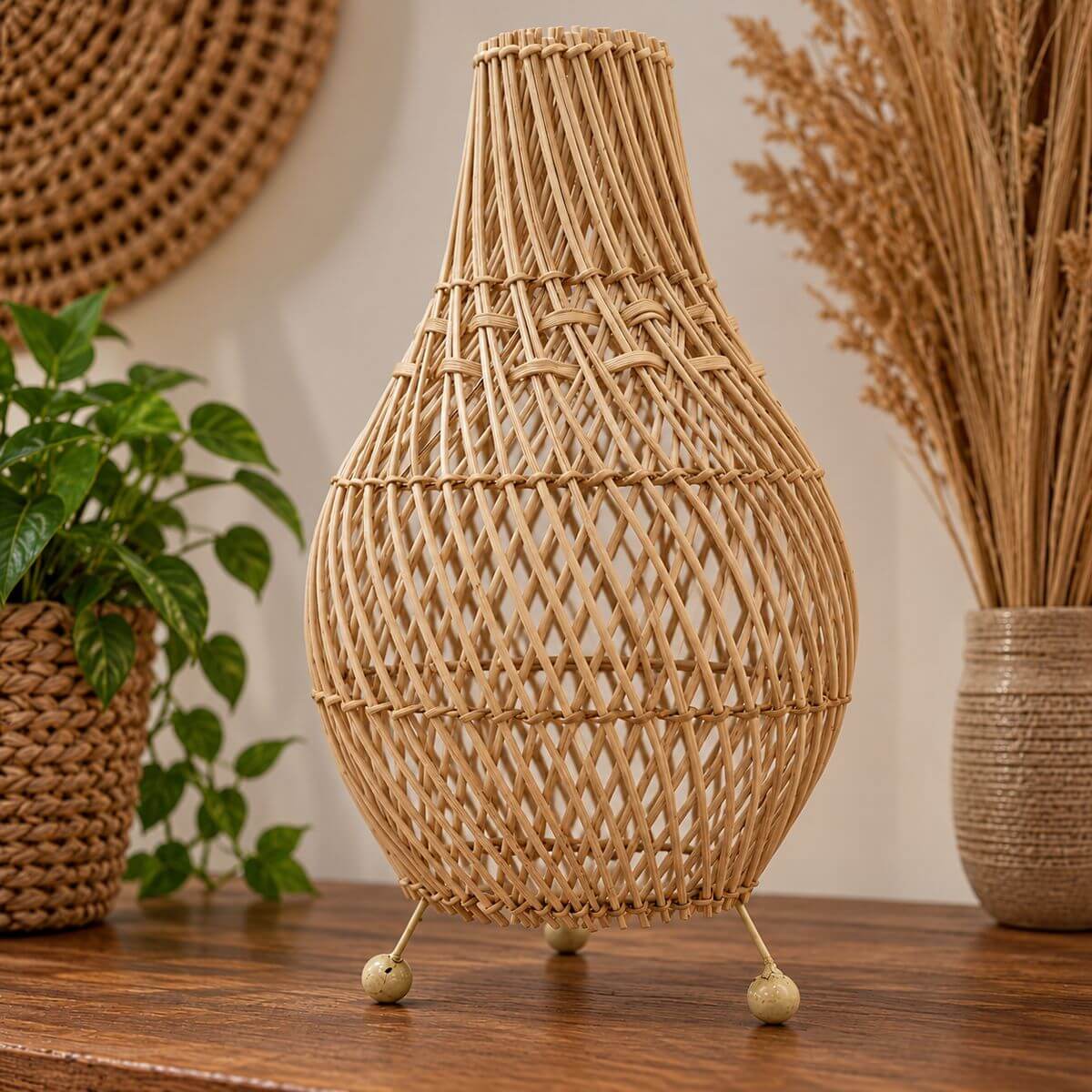 Lampe de table en rotin naturel tressé, forme ventrue sur trois pieds, posée sur un buffet en bois