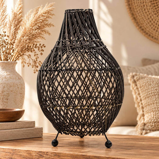 Lampe de table en rotin noir tressé en spirale, liens beiges, posée sur une console en bois près d’un vase de pampa