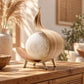 Lampe bohème en feuille de coco éteinte, sur quatre pieds en bois clair
