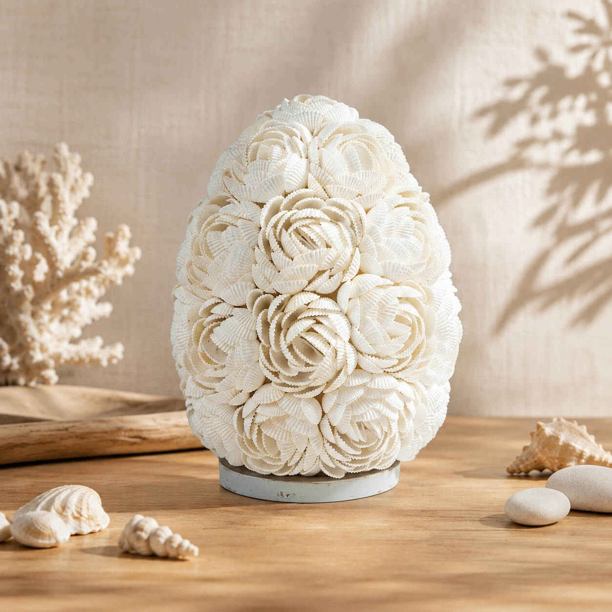 Lampe œuf en coquillages roses marines sur socle clair dans un décor bord de mer.