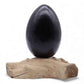 Lampe œuf de lave gris anthracite éteinte sur socle bois flotté brut sur fond blanc.