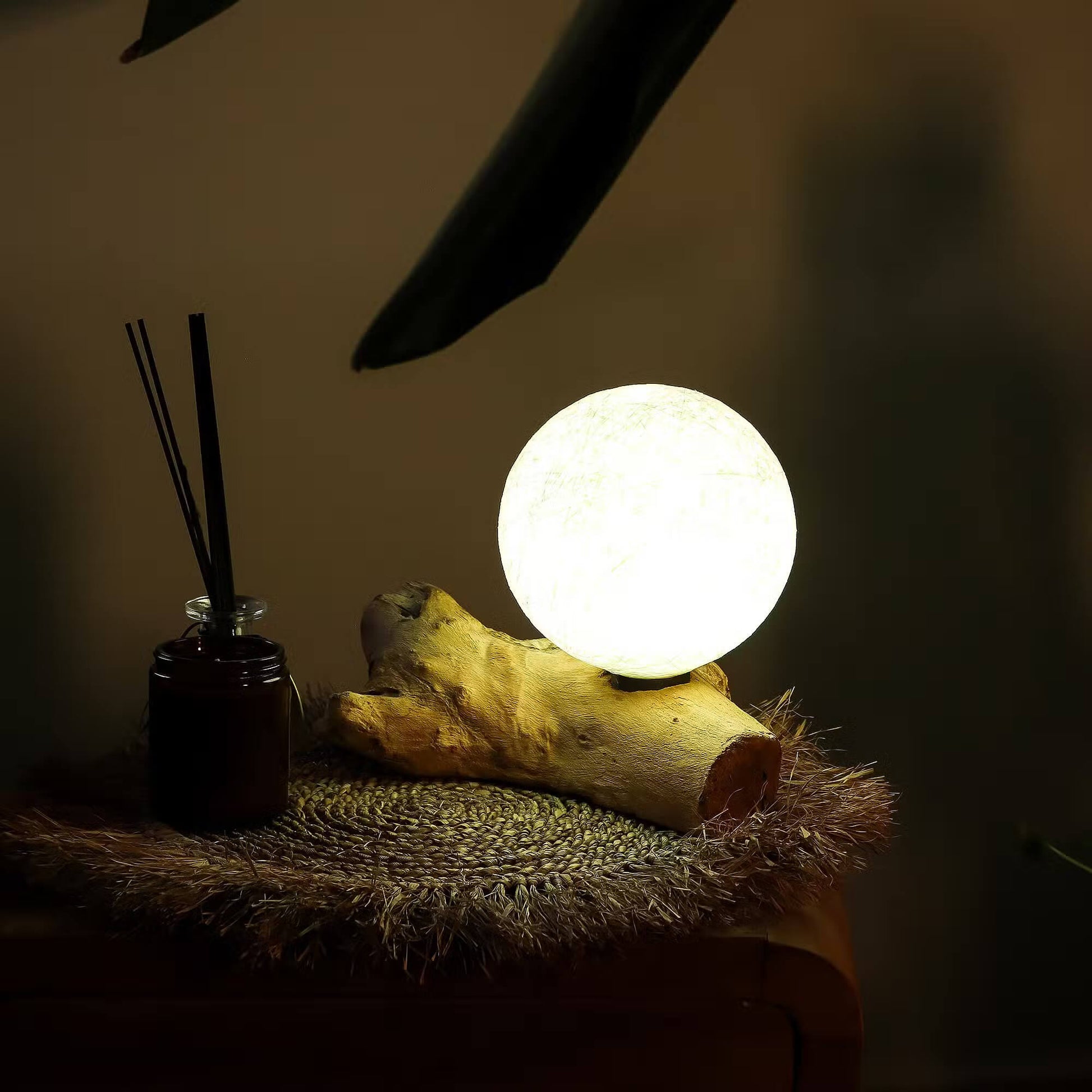 Lampe sphère lune ivoire allumée en décoration zen avec diffuseur sur meuble en bois.