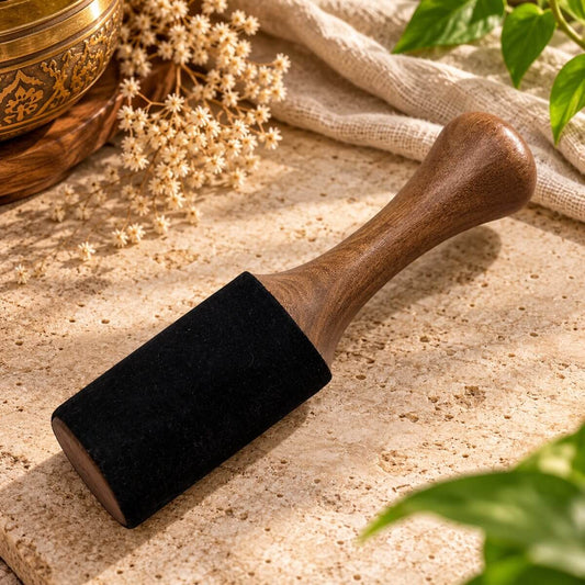 Maillet roi en bois pour bol tibétain, tête gainée de noir et manche galbé, posé sur une pierre claire près d’un bol doré