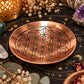 Plateau rond en cuivre poli gravé d'une fleur de vie aux lignes noires, posé sur une nappe noire aux motifs de lune