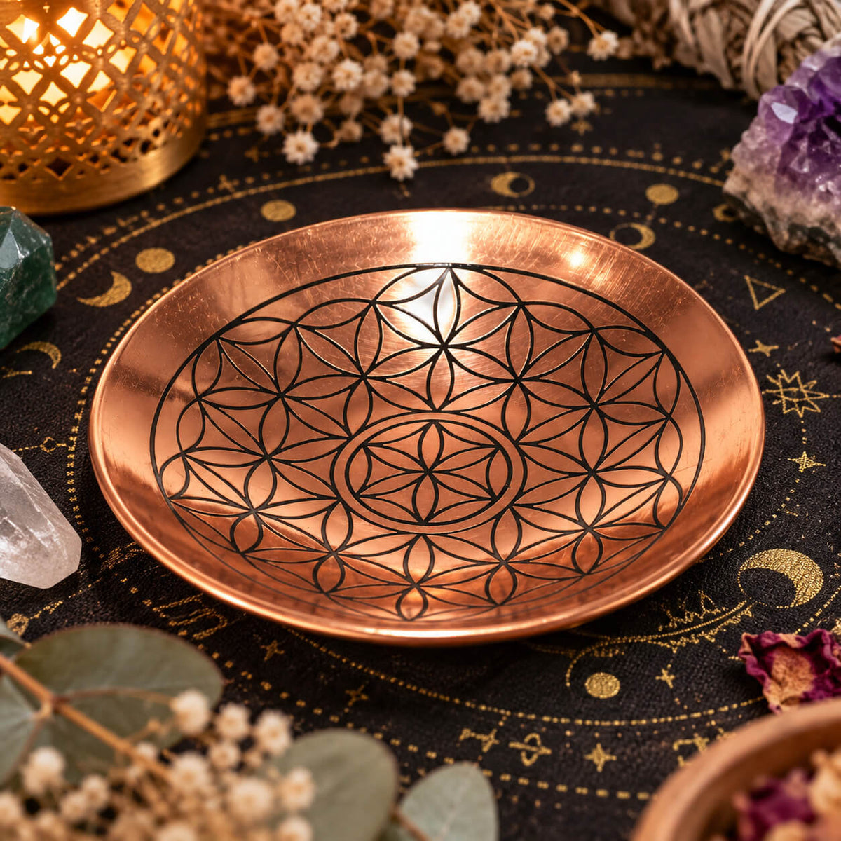 Plateau rond en cuivre poli gravé d'une fleur de vie aux lignes noires, posé sur une nappe noire aux motifs de lune