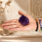 Pointe d'améthyste naturelle tenue dans une main avec bracelets en pierres naturelles.