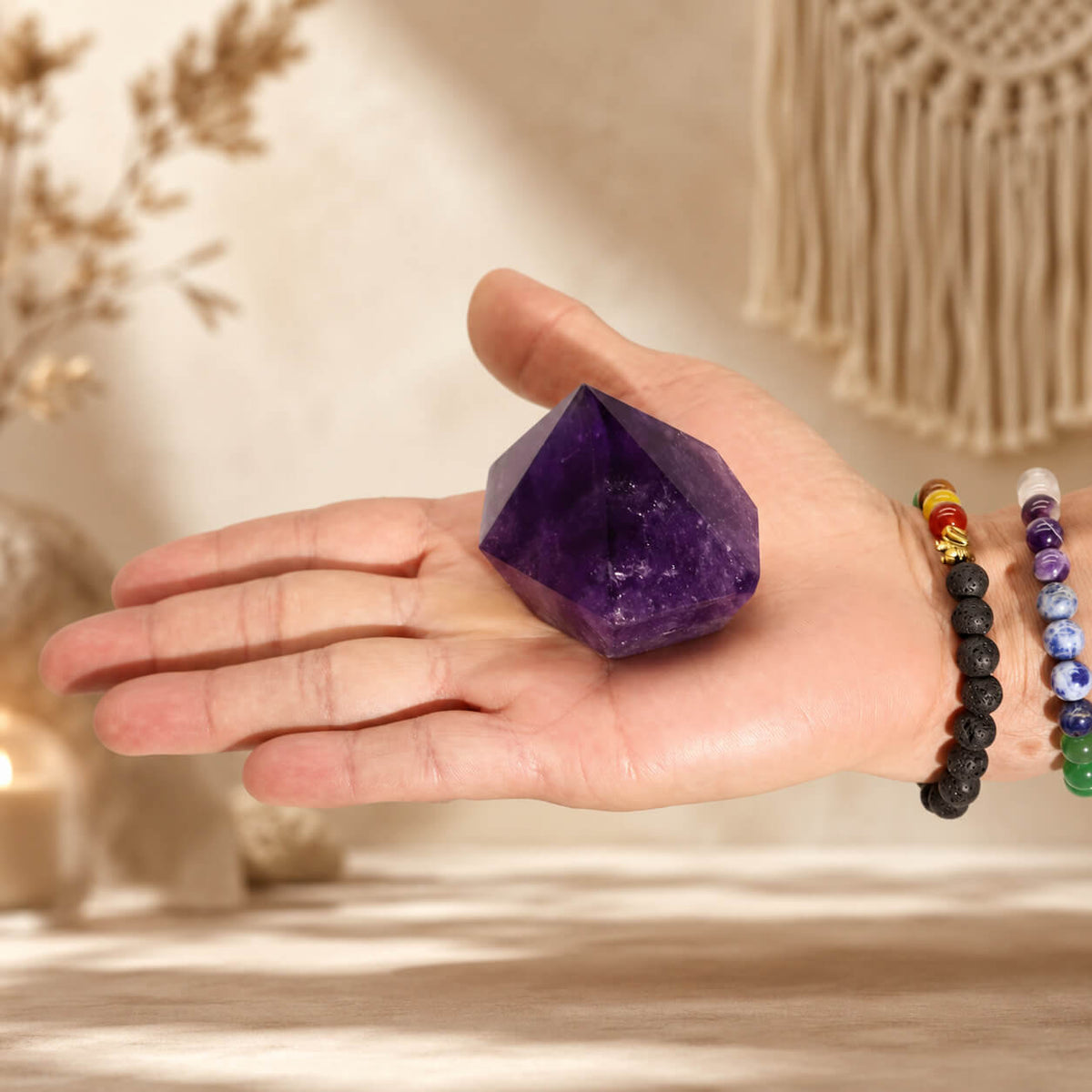 Pointe d'améthyste naturelle tenue dans une main avec bracelets en pierres naturelles.