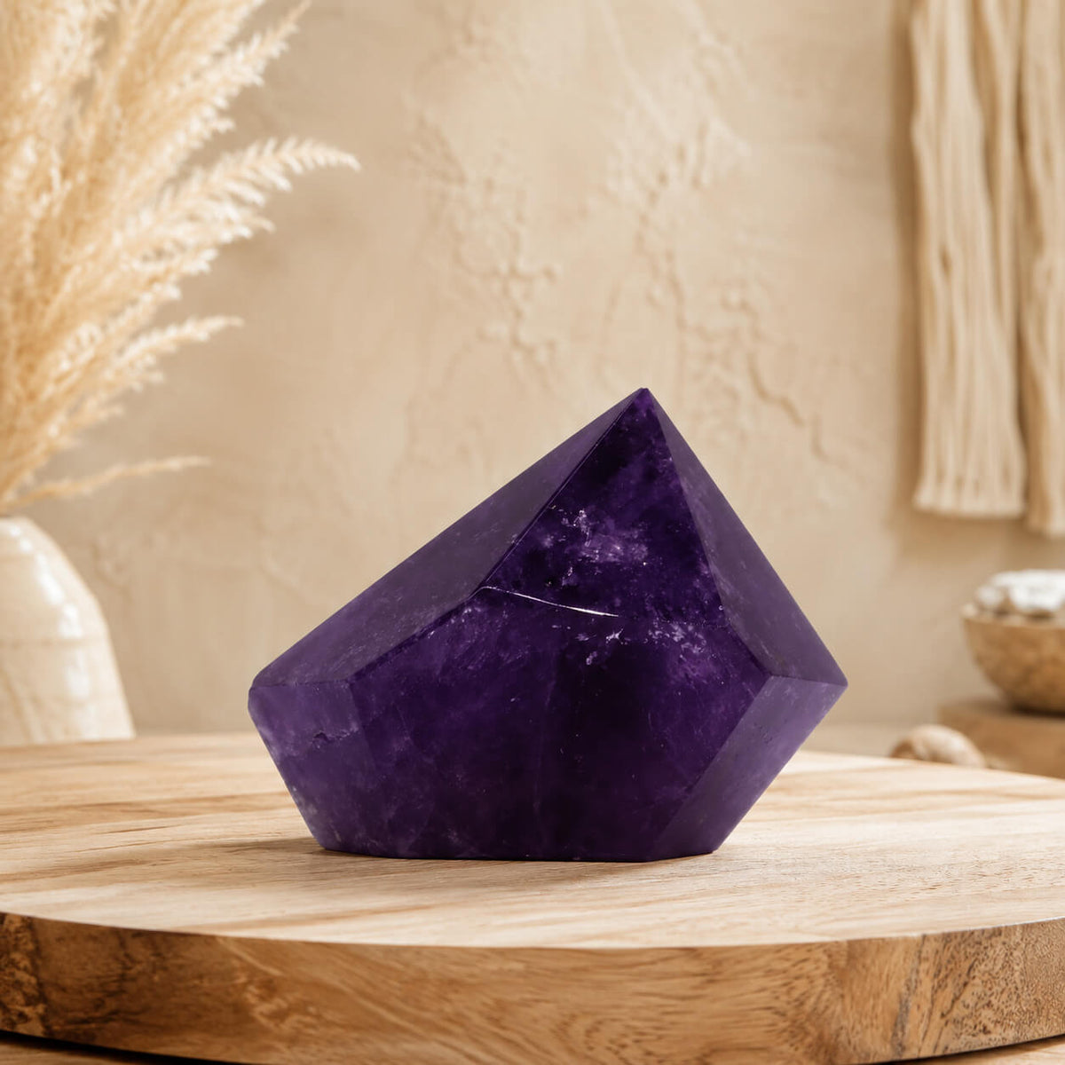 Pointe d'améthyste naturelle violette posée sur table en bois avec plantes séchées.