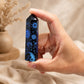 Pointe d'obsidienne noire gravée tenue entre les doigts, motifs soleil et lune bleu