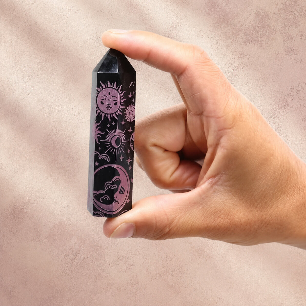Pointe d'obsidienne noire gravée tenue entre les doigts, motifs soleil et lune roses
