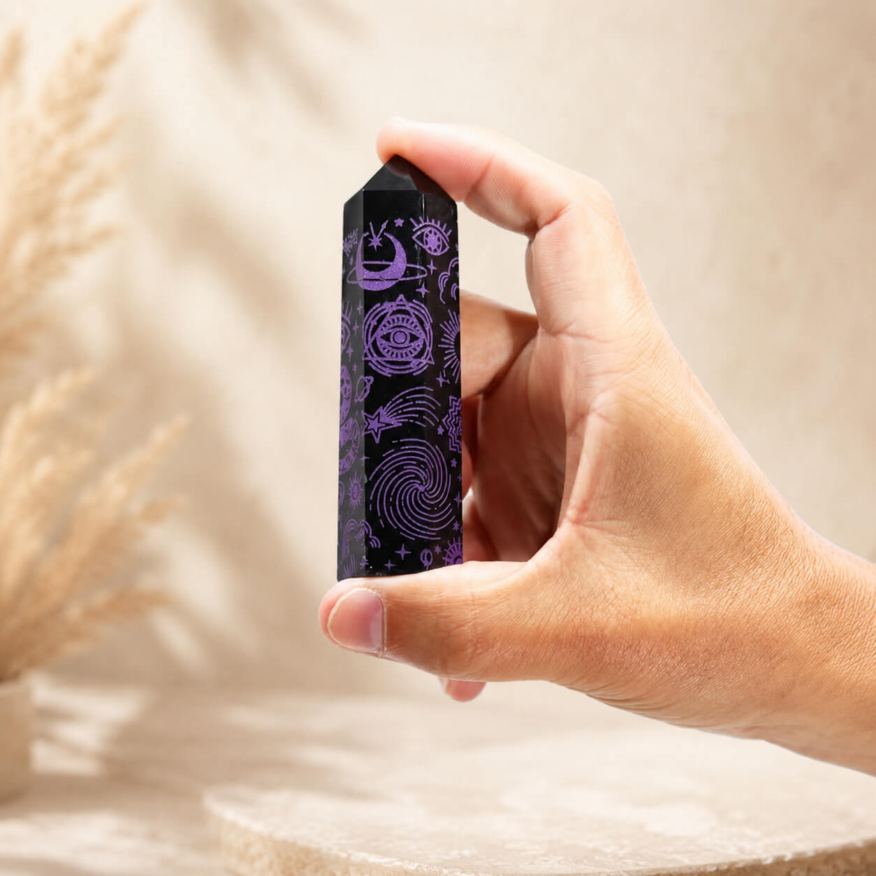 Pointe d'obsidienne noire gravée d'une galaxie en spirale et d'un œil mystique en violet, tenue en main