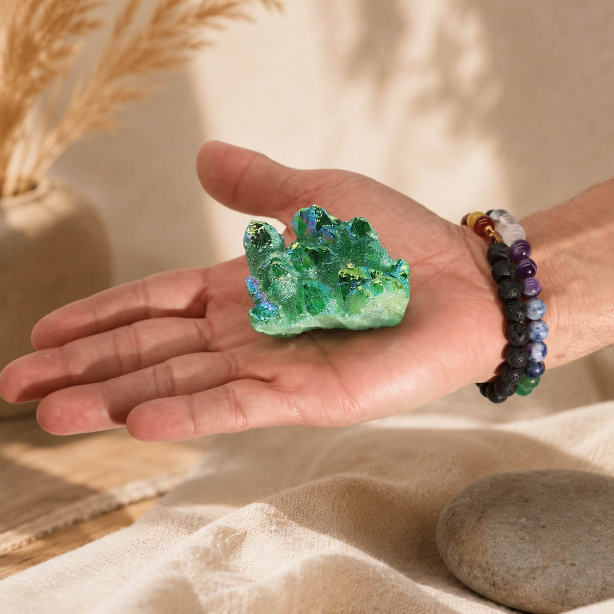 Quartz Aura Flamme Verte aux reflets émeraude irisés tenu dans une main avec bracelets en pierres