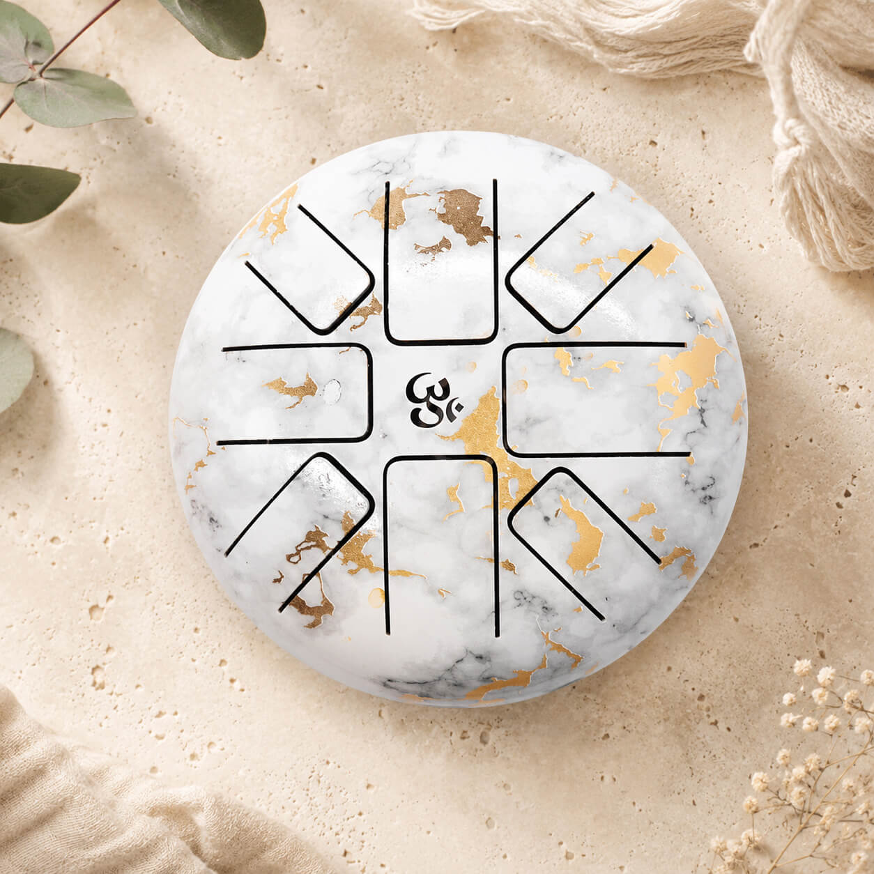 Vue de dessus du tongue drum marbré blanc et or 18cm révélant les huit langues mélodiques en acier et la signature Om centrale dorée.