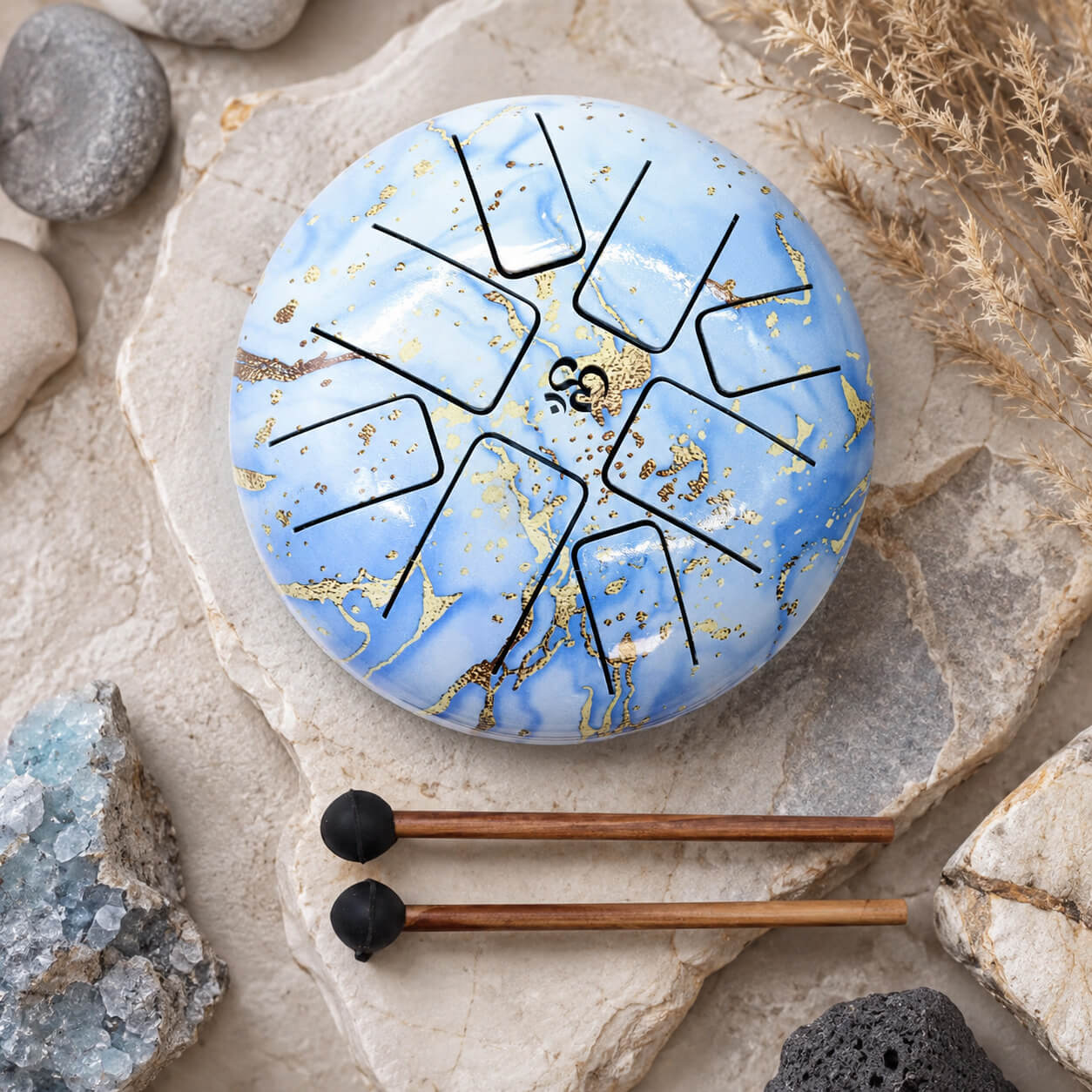 Tongue drum 18cm bleu ciel veiné d'or avec symbole Om et deux mailloches en bois sur pierre naturelle.