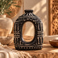 Vase ovale percé en terre cuite brun foncé à décor crème, posé sur une table en bois près d'un panneau sculpté