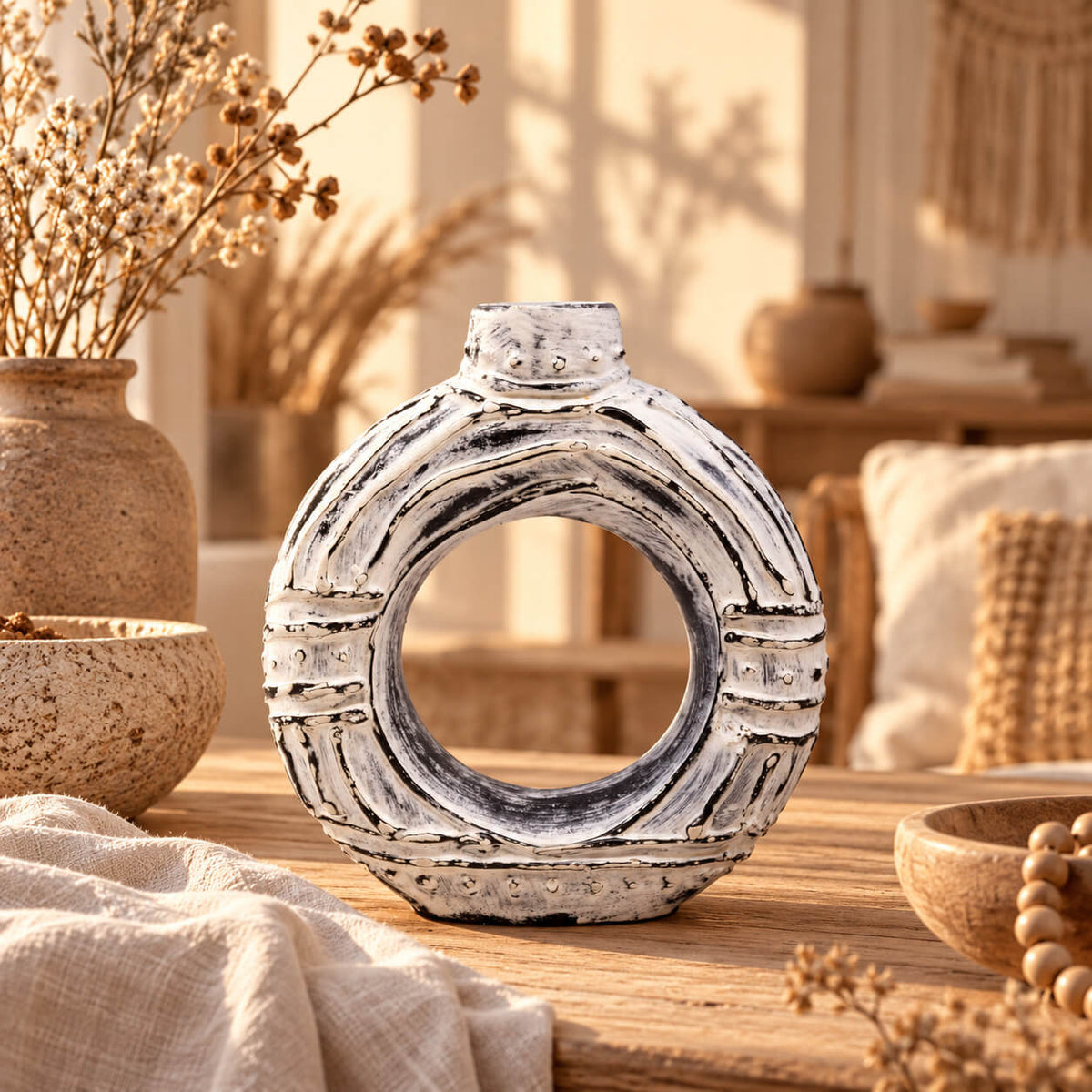 Vase anneau en terre cuite crème patinée de noir, ouverture centrale et petit col, sur une table en bois