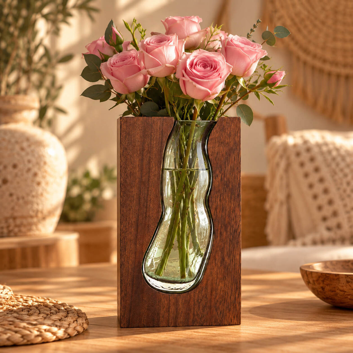 Vase terrarium en verre ondulé dans un bloc de bois foncé, garni de roses roses et de feuillage dans l'eau